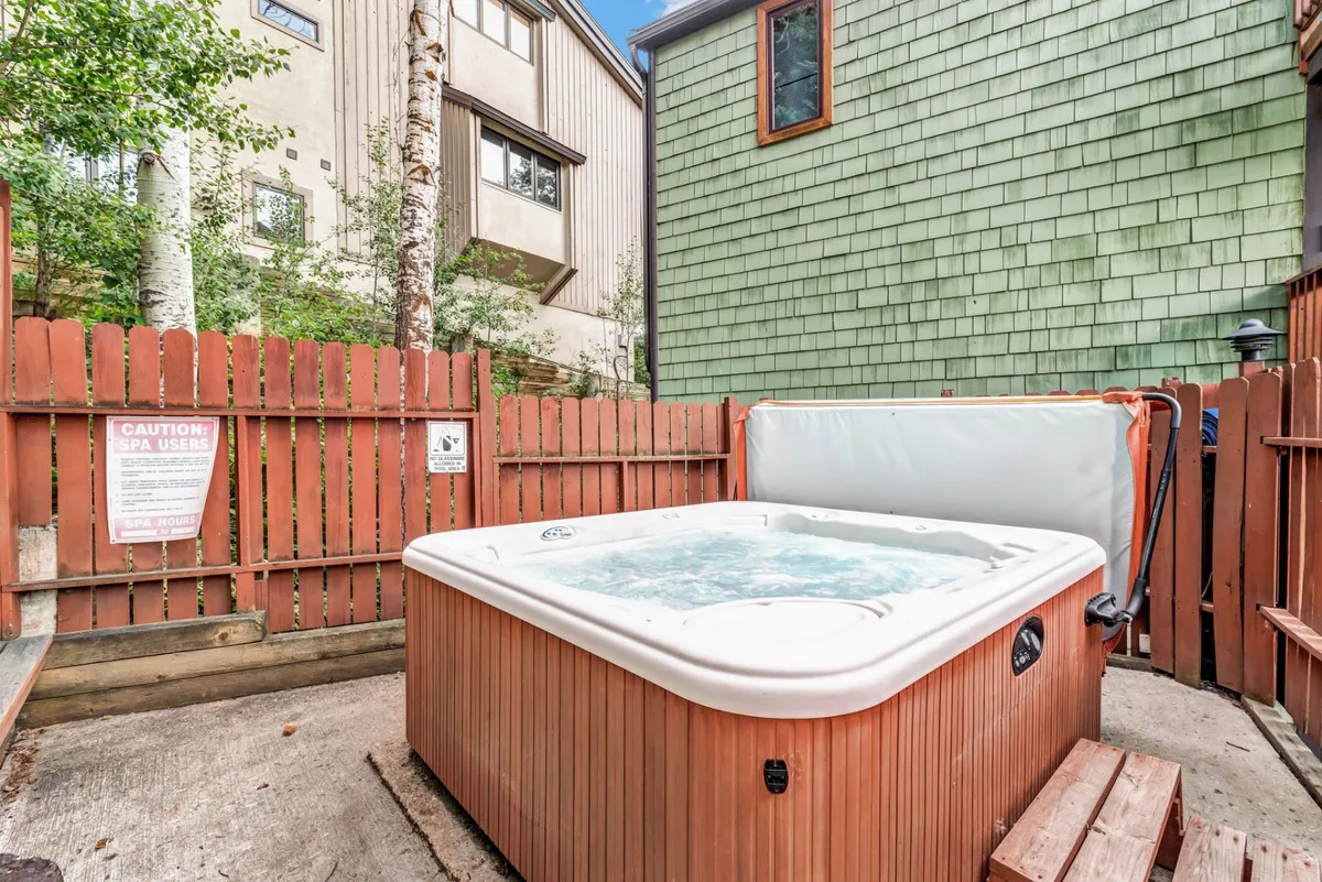 An outdoor hot tub nestled amid leafy greenery, partially surrounded by a wooden privacy fence. The area feels cozy and intimate—ideal for relaxing after a day of mountain adventure. There’s space for several people to enjoy the hot tub together, with natural elements enhancing a sense of tranquility.