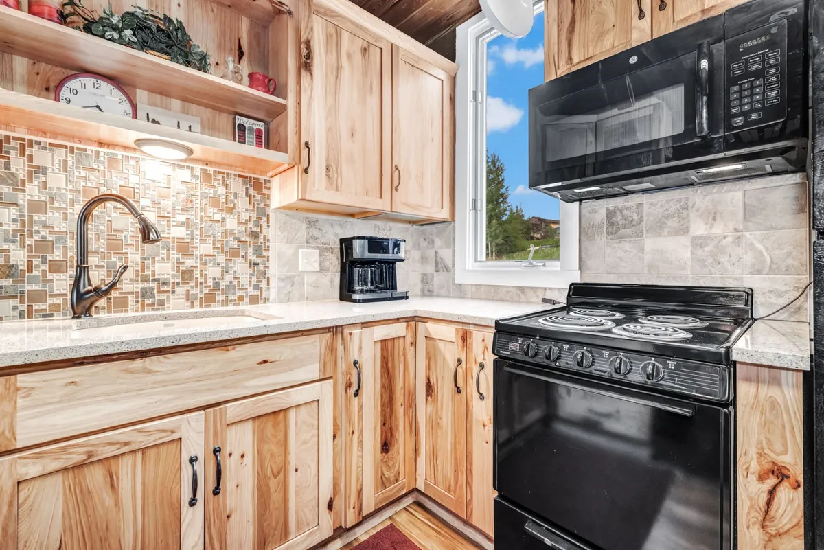 A close view of a kitchen focused on natural wood cabinetry, modern appliances, and a textured backsplash. The warm lighting and inviting setup make the space ideal for cooking and family gatherings.