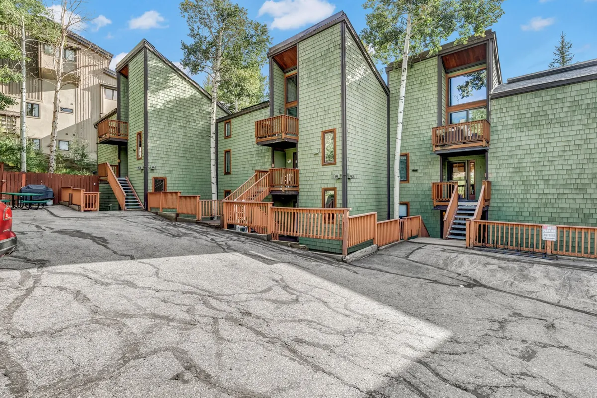 An exterior perspective of the condo community showing green shingle siding, multiple wooden balconies, and aspen trees, all bathed in natural light. The scene feels tranquil and welcoming, hinting at the relaxing end to a day of family activity.