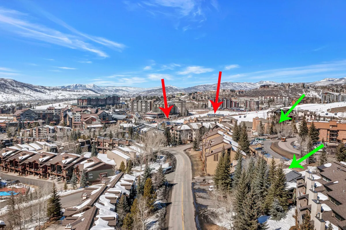 A tranquil view of snow-covered rooftops nestled among tree-lined streets with towering mountains in the background. Residential buildings dot the landscape, suggesting a welcoming and active community set in a beautiful alpine environment.