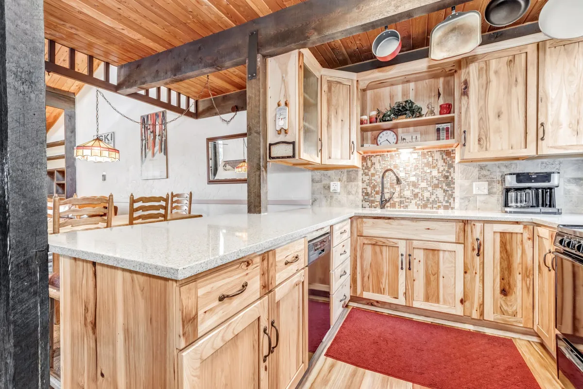 This image highlights a warm and welcoming kitchen interior featuring a granite countertop, wood cabinetry, a decorative backsplash, and stainless steel appliances. The open layout creates a seamless flow to adjacent living spaces, supporting group cooking and gatherings.