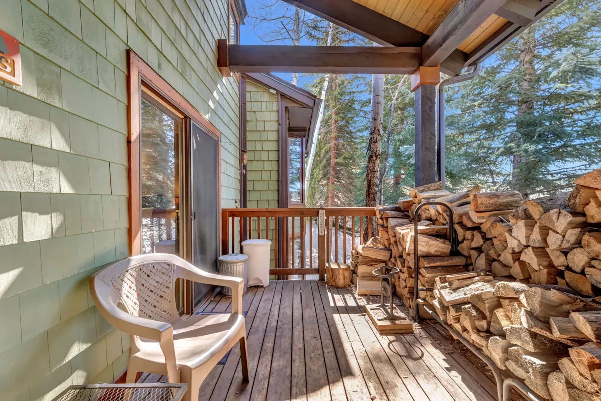 This exterior image showcases a private wooden deck with stacked firewood, a lawn chair, and a wooden railing, surrounded by evergreens. The outdoor setting is tranquil and inviting, perfect for morning coffee or sunset drinks as described in the section.