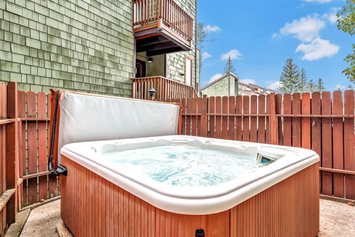 An inviting view of an outdoor hot tub, enclosed by a wooden fence for privacy, with a balcony above. The scene suggests a relaxing soak after a day on the slopes, reflecting the après-ski experiences described in the content.